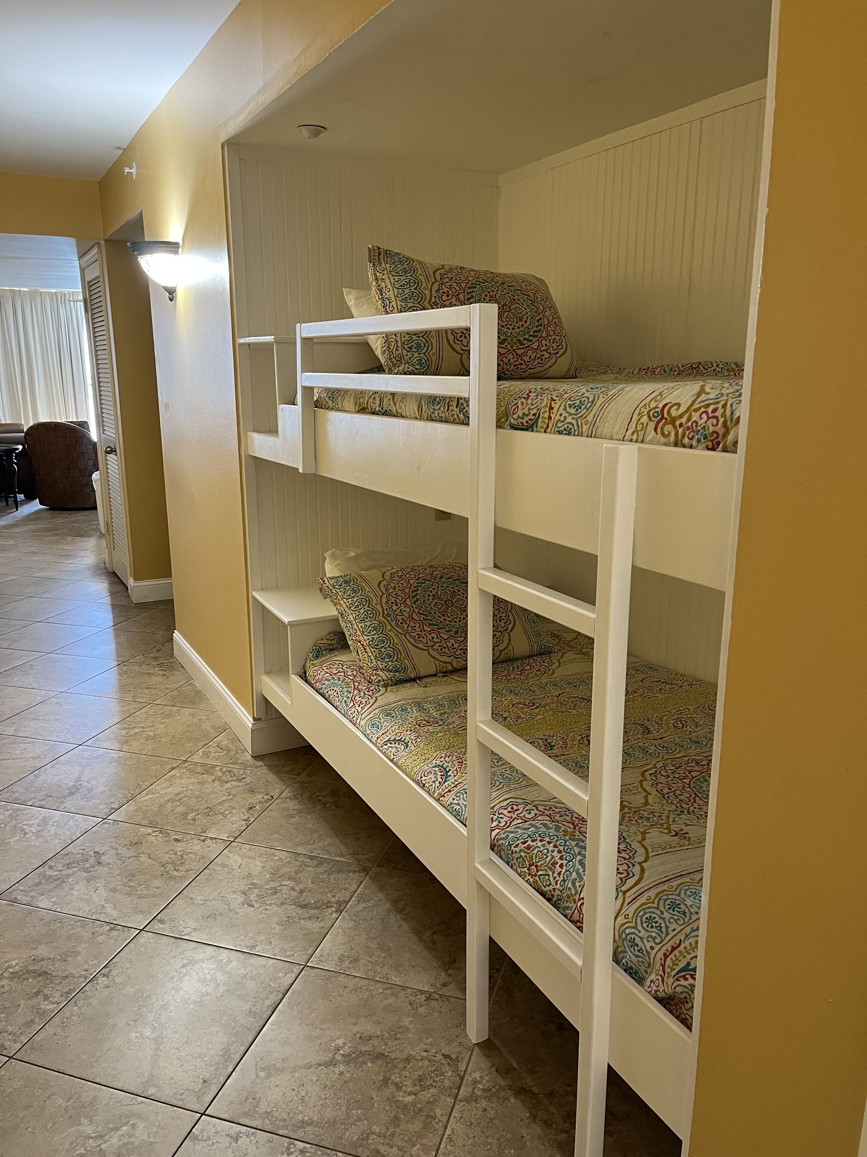 A bunk bed with patterned bedding in a room with beige walls and tiled flooring.