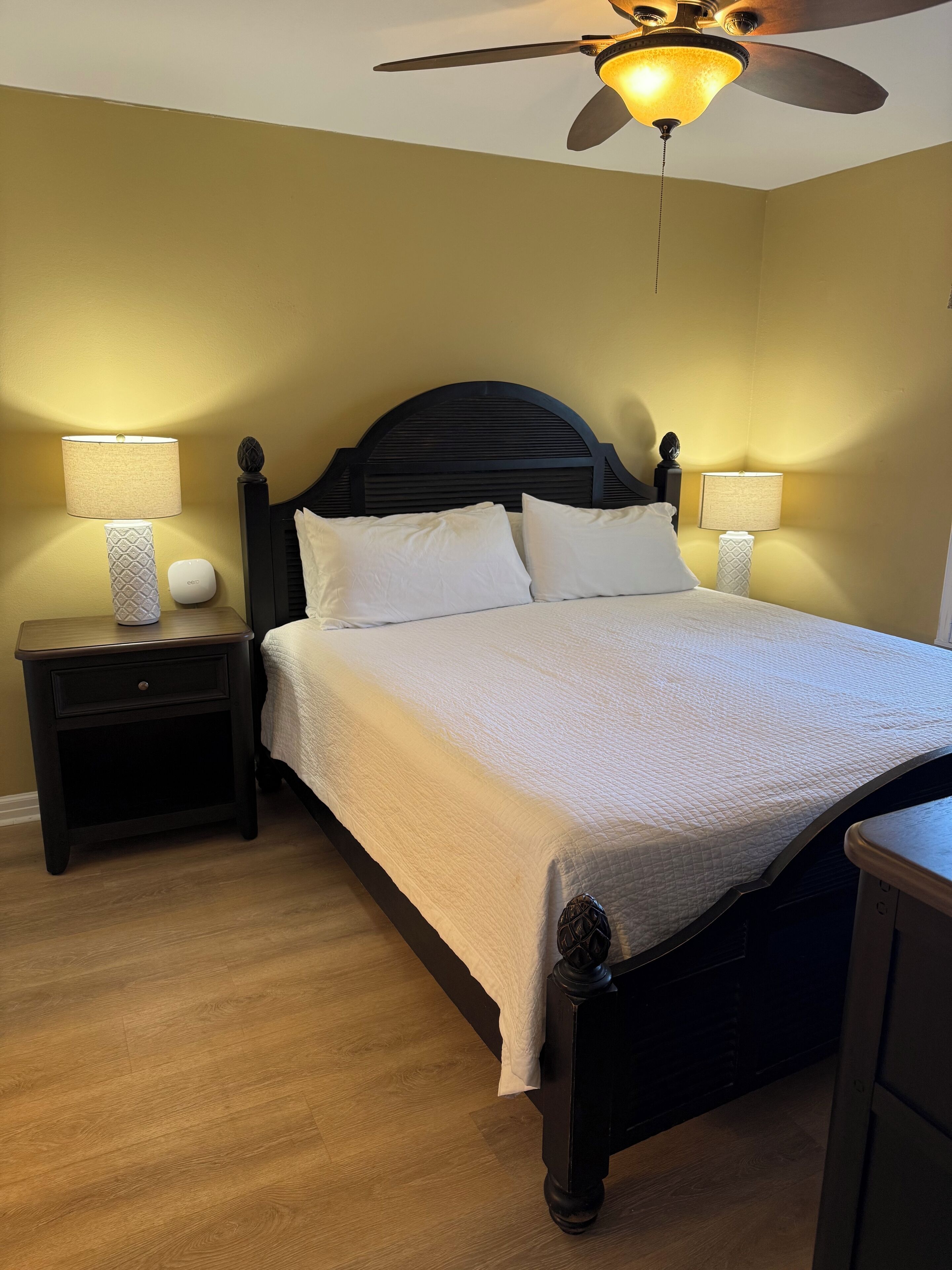 A neatly made bed with white linens, two bedside tables with lamps, and a ceiling fan.
