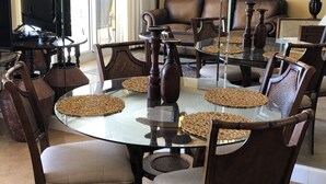 Een eetruimte met een ronde glazen tafel, houten stoelen en geweven placemats.