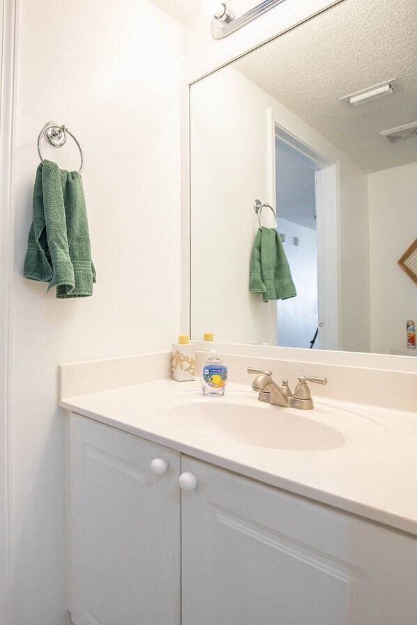 A bathroom with a white sink, a mirror, and two green towels hanging on towel rings. - BeachFRONT!! 65" HD TV, WIFI, Netflix, and View! (Fort Walton Beach)