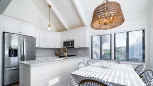 A modern kitchen with white cabinetry, stainless steel appliances, a large island, and a dining area with wicker chairs. - Bright Decor! 3 BR/3 BA Villa; Pools/Beach Nearby! Amenity access included! (Seabrook Island)