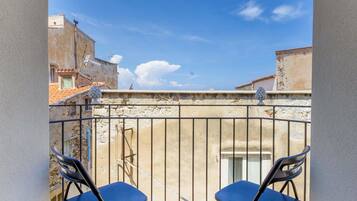 Un balcon avec deux chaises bleues, un sol carrelé et une vue sur des immeubles sous un ciel dégagé.