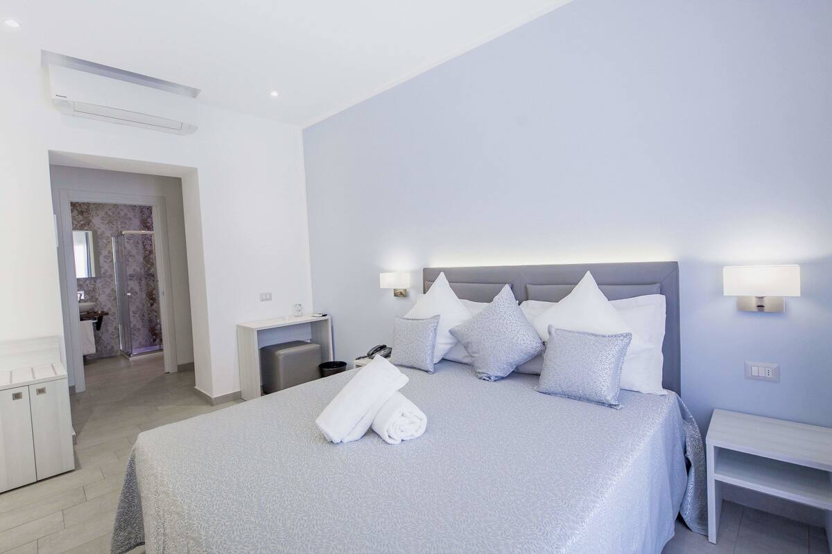 Una habitación de hotel moderna con una cama bien hecha, una mesita de noche y un pequeño escritorio con lámpara.