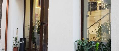 The exterior of Ossuna Bay hotel boutique with a large glass entrance, potted plants, and a sign above the door.