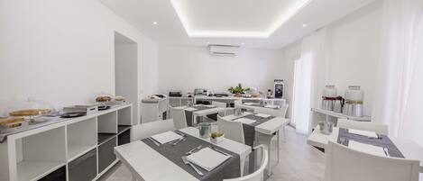 Un comedor moderno con mesas y sillas blancas, una estación de servicio central, y un techo luminoso y bien iluminado.