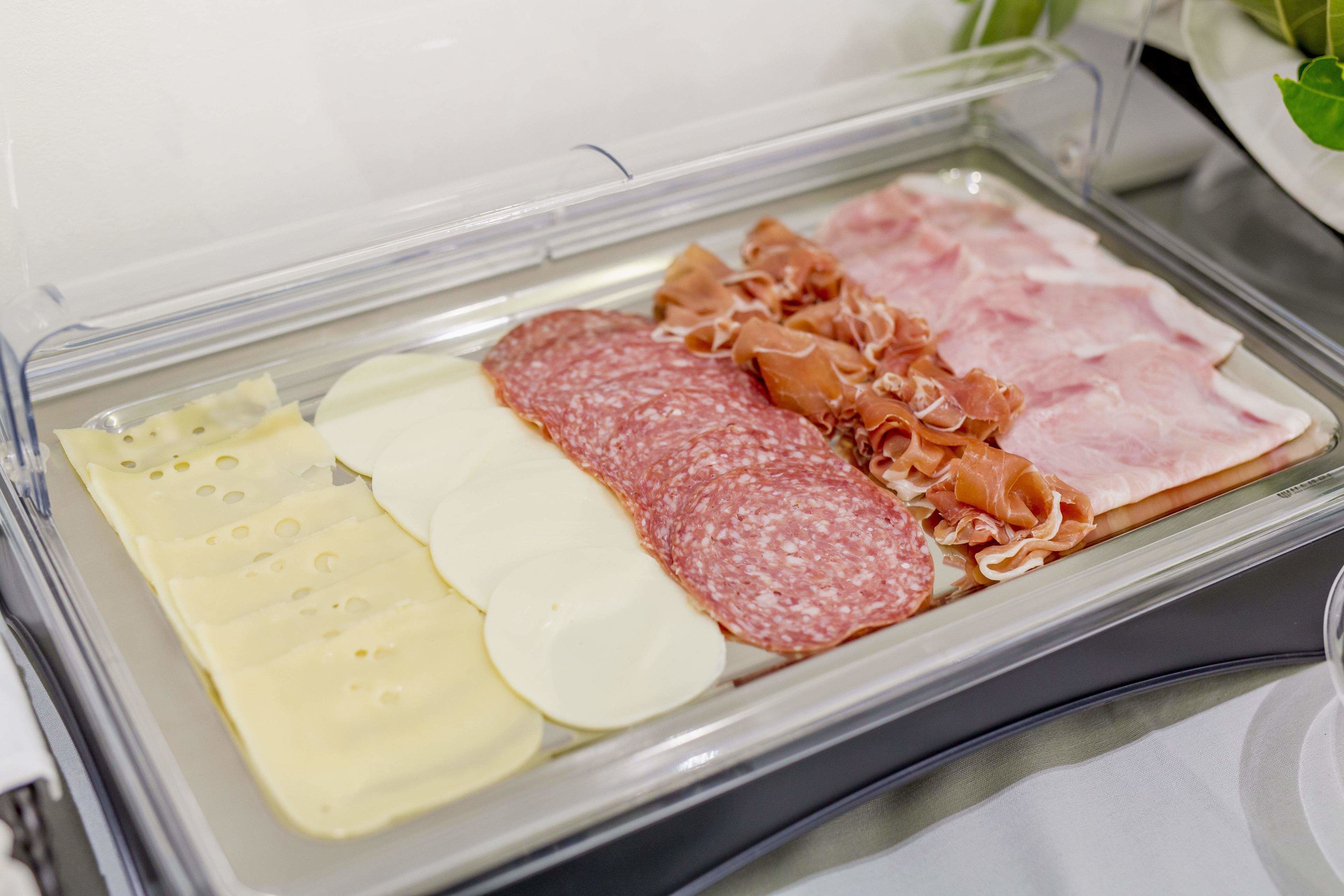 Un recipiente transparente con varios tipos de queso y embutidos curados.