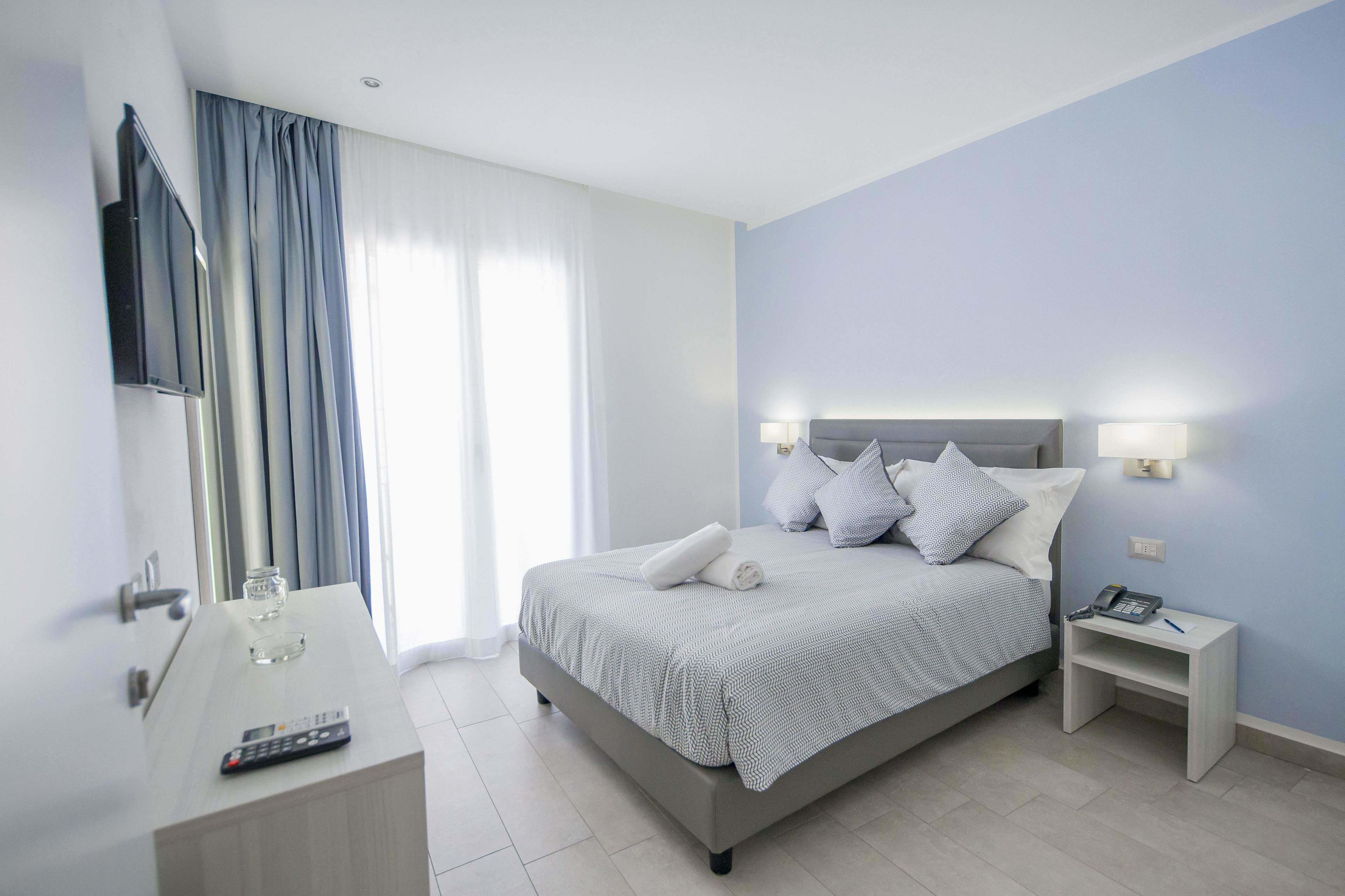 A modern hotel room with a bed, bedside table, and a desk with a remote control.