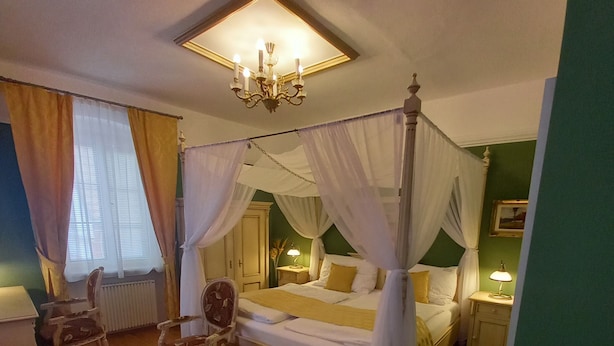 A four-poster canopy bed with a nightstand, a chair, and a table in a room with wooden flooring and green walls. - Pension PREMIUM (Cesky Krumlov)