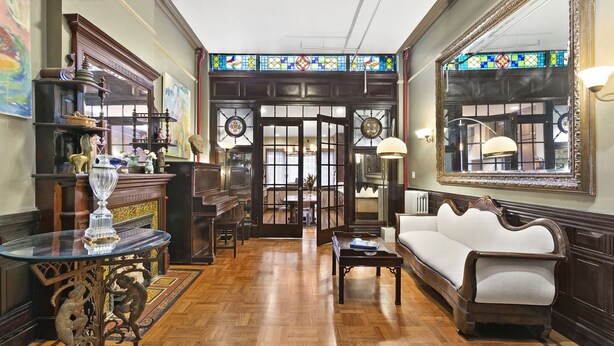 A room with a piano, a sofa, a table with a vase, and a large mirror. - Northern Lights Mansion (New York)