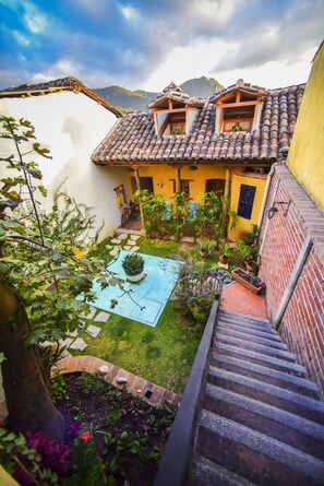 Une cour avec une piscine, des plantes en pot et un escalier menant à un bâtiment doté d’un toit en tuiles.