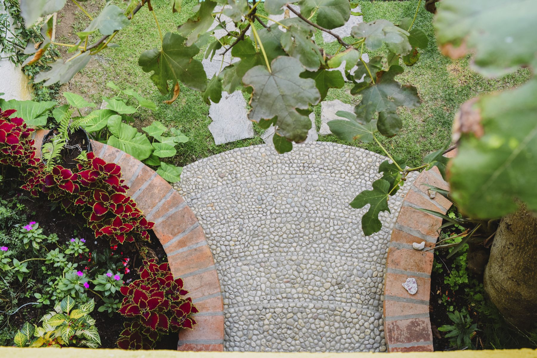 A garden with a pebble pathway, a brick archway, and various plants.