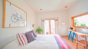 A bedroom with a bed, colorful pillows, a desk, a bicycle drawing on the wall, and a window with a view. - Casa Francisco (San Cristóbal de las Casas)