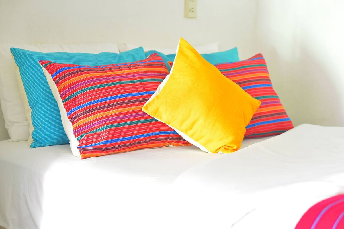 Een bed met witte beddengoed en kleurrijke gestreepte kussens.