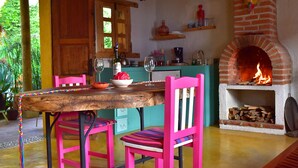 A rustic kitchen with a brick fireplace, wooden table, and pink chairs. - Casa Francisco (San Cristóbal de las Casas)