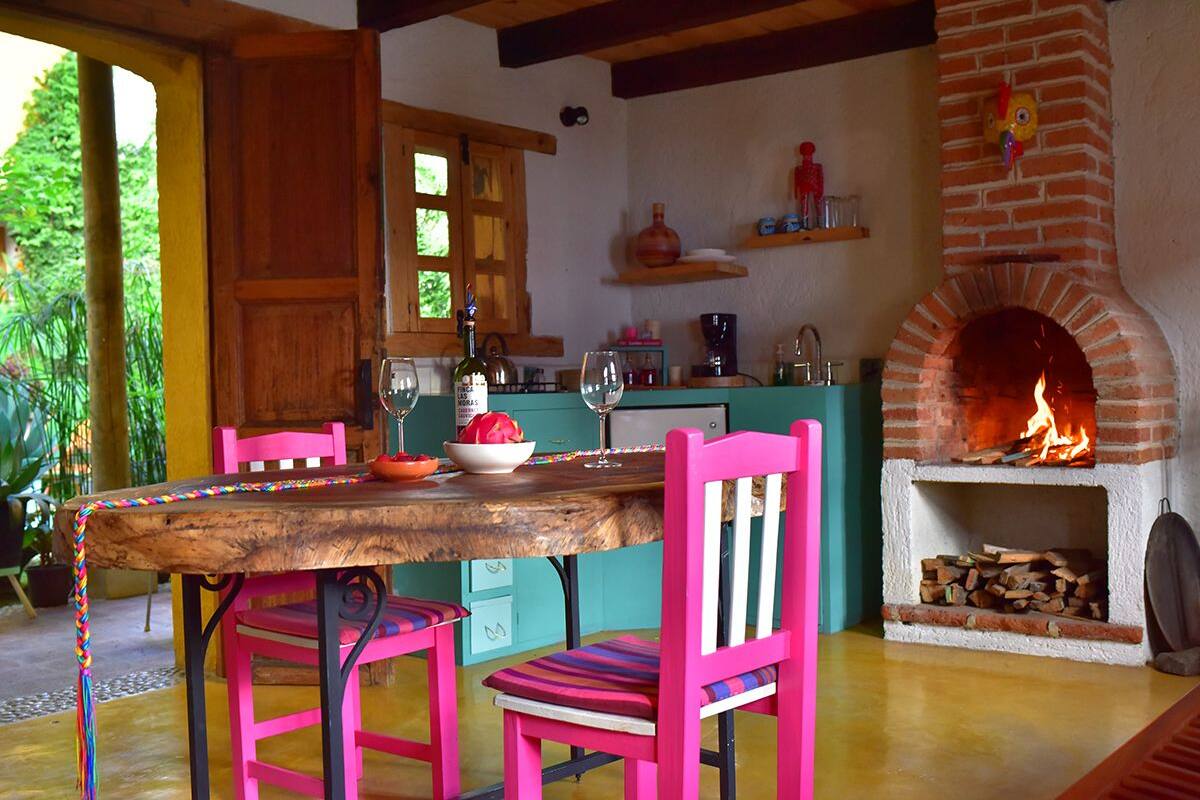Een rustieke keuken met een bakstenen openhaard, een houten tafel en roze stoelen.