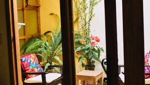 A room with a wooden door frame, a bed with a colorful pillow, a chair, a small table, and a potted plant. - Casa Francisco (San Cristóbal de las Casas)