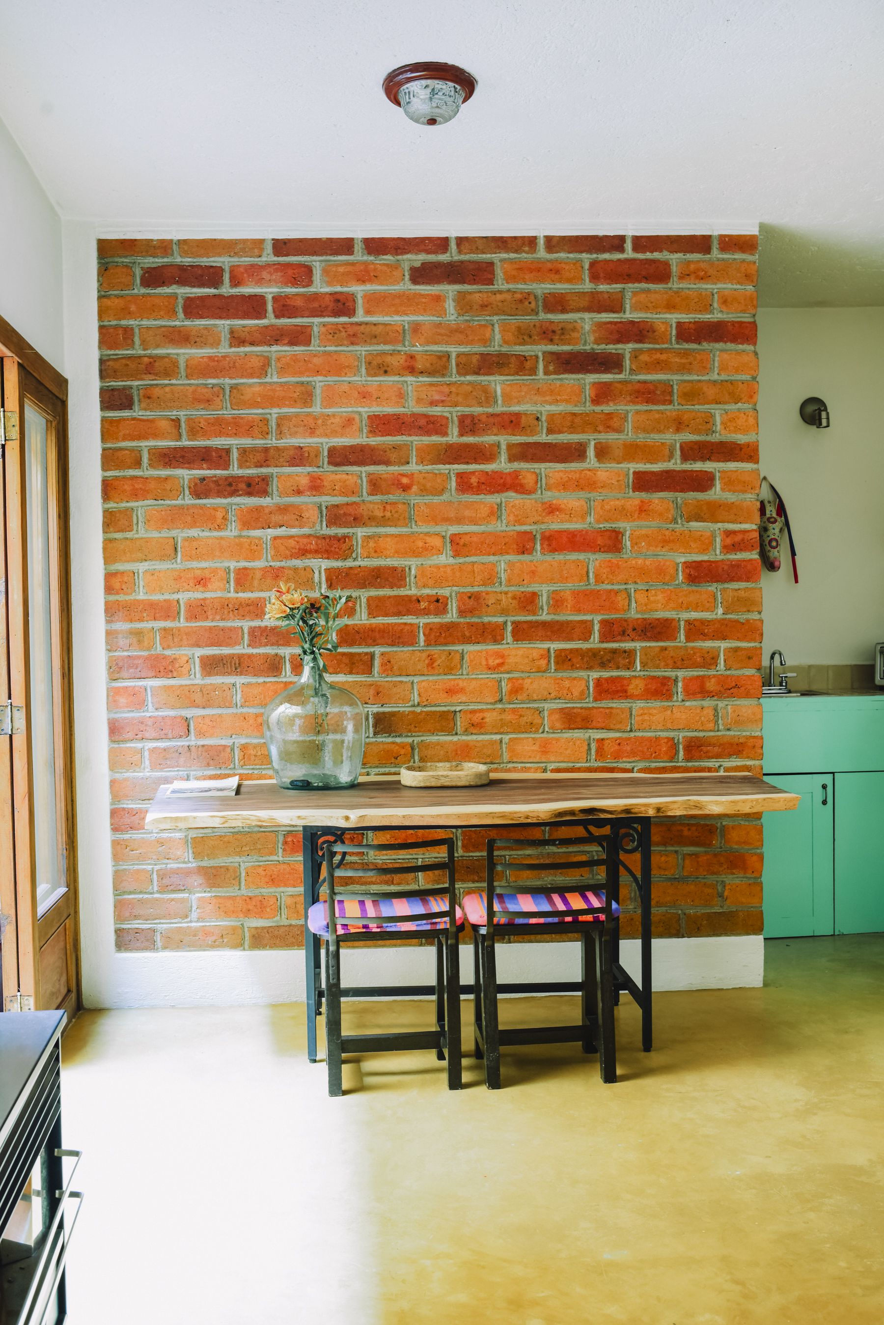 A kitchen with a brick wall, a wooden table, a bench, and a vase with flowers.