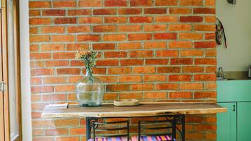A kitchen with a brick wall, a wooden table, a bench, and a vase with flowers.