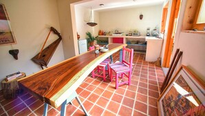 A dining area with a wooden table and pink chairs, a kitchen in the background, and a tiled floor. - Casa Francisco (San Cristóbal de las Casas)