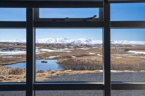 A window view of a landscape with snow-covered mountains, a small body of water, and a road. - Skulagardur (Skinnastadur)