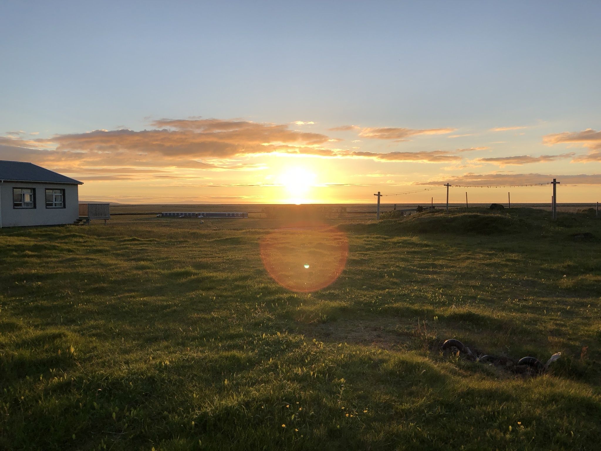 Un campo cubierto de hierba con una casa y una vía de tren a lo lejos.