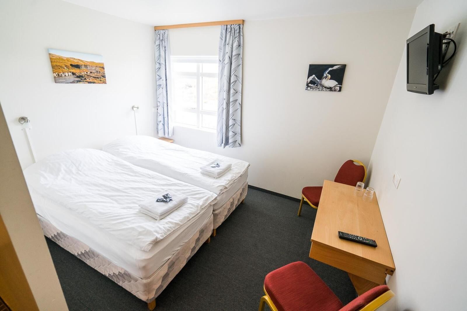 Een hotelkamer met twee bedden, een bureau, een stoel, een televisie en kunstwerken aan de muur.