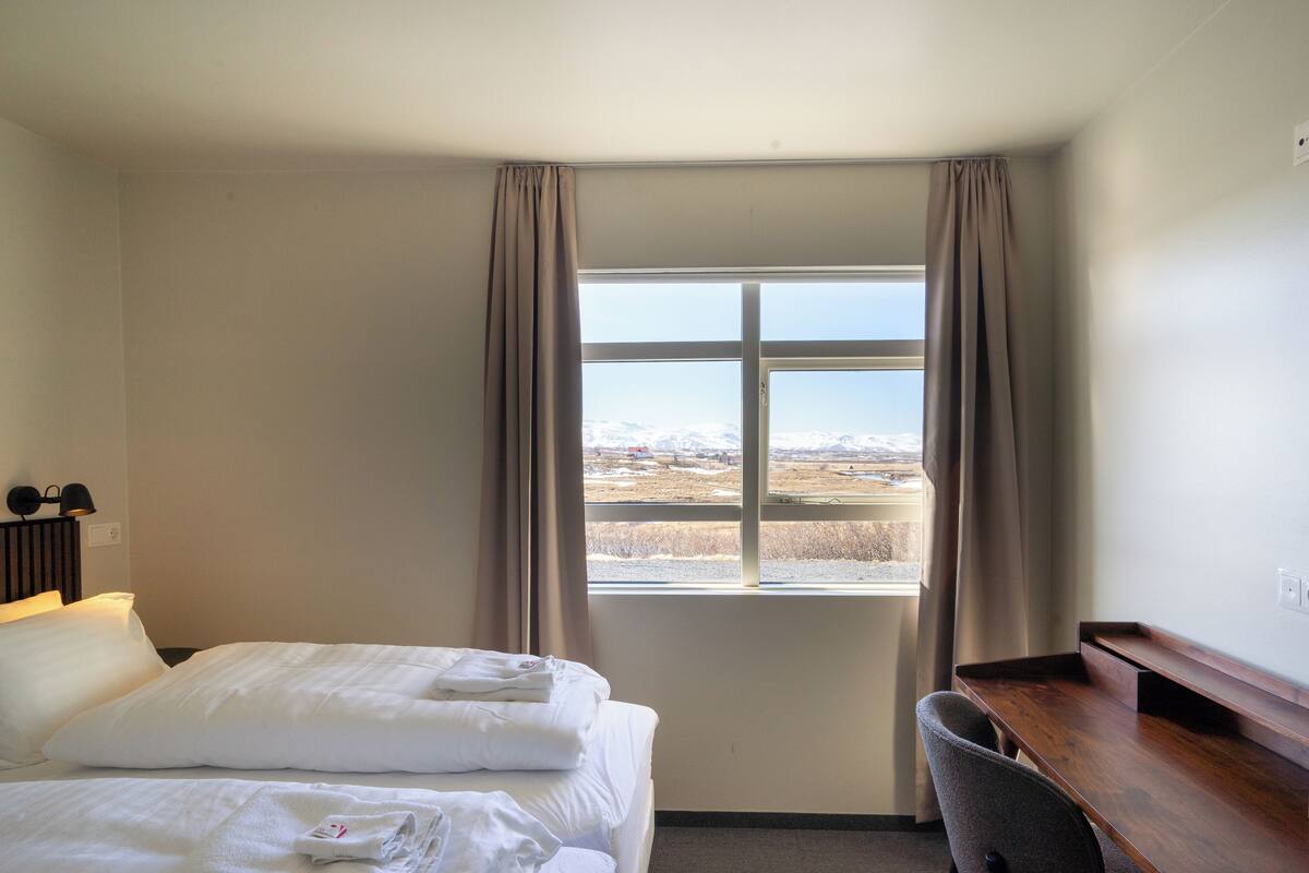 Habitación de hotel con cama, escritorio y ventana con vista al paisaje.