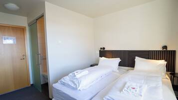 A hotel room with two beds, a wooden door, a toilet, and a nightstand with a lamp.