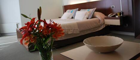 Ein Hotelzimmer mit Bett, Nachttisch, Lampe und einer Blumenvase.