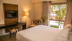 A hotel room with a bed, a desk with a chair, a TV mounted on the wall, a lamp, a window with curtains, and a view of the outside. - Hotel Costa Real (La Serena)