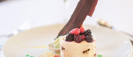 Un postre con bayas y una hoja de chocolate sobre un plato blanco.