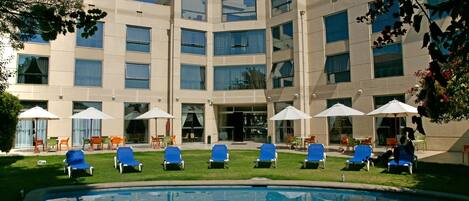 Een modern hotel met een zwembad, terras en een groot gebouw met veel ramen.