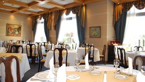 A dining area with multiple tables set for service, wooden ceiling beams, and large windows with curtains. - Hotel Costa Real (La Serena)
