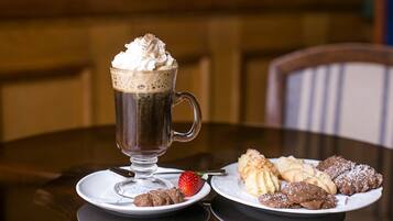 A dessert setting with a glass mug of a dark beverage topped with whipped cream and a strawberry, accompanied by plates of assorted pastries.