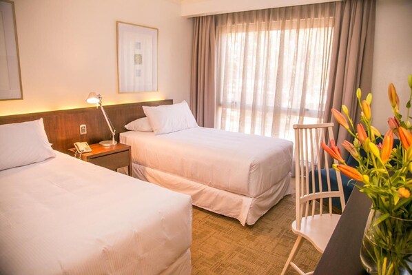 A hotel room with two beds, a bedside table with a lamp, a chair, and a vase with flowers. - Hotel Costa Real (La Serena)