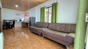 Una sala de estar con sofá, un comedor con sillas, una cocina con electrodomésticos y una ventana con cortinas.