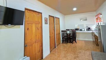 A compact living space with a kitchen area, wooden doors, a flat-screen TV, and a dining table with chairs.