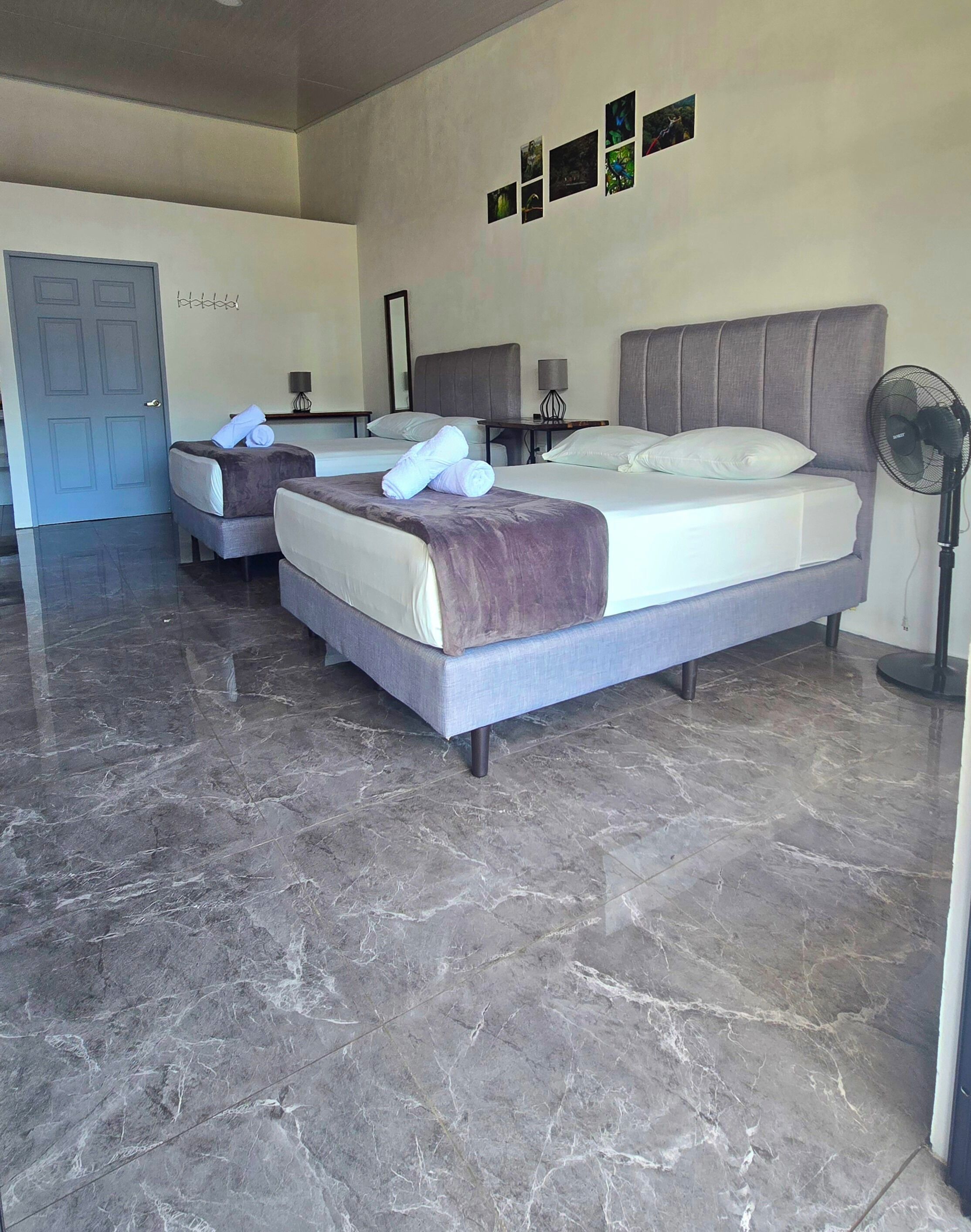 A hotel room with two beds, marble flooring, a door, and a wall with framed pictures.