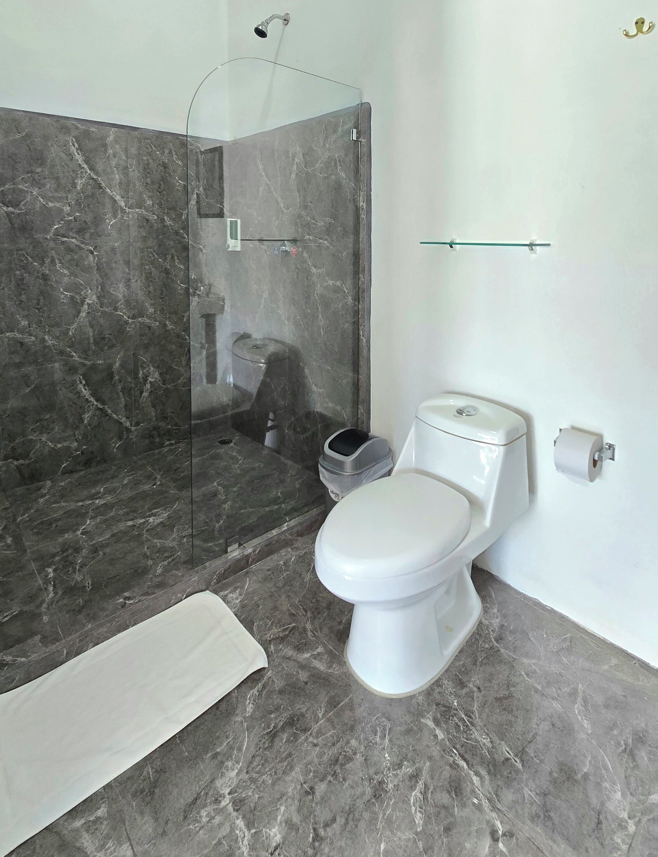 A bathroom with a toilet, a shower, and a marble floor.