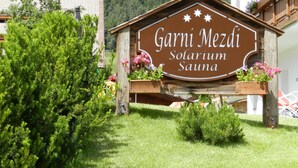 A wooden sign for Garni Mezdi Solarium Sauna with a mountainous backdrop. - Garni Apartments Mezdi (Selva di Val Gardena)