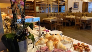 A restaurant with tables set for dining, a buffet with pastries, and a decorative plant. - Garni Apartments Mezdi (Selva di Val Gardena)