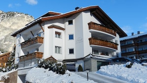 A multi-story hotel with balconies, a stone facade, and a mountain backdrop. - Garni Apartments Mezdi (Selva di Val Gardena)