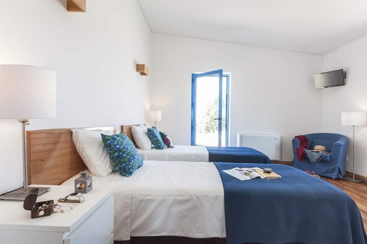 A hotel room with two beds, a desk, a chair, a TV, and a window with a view.
