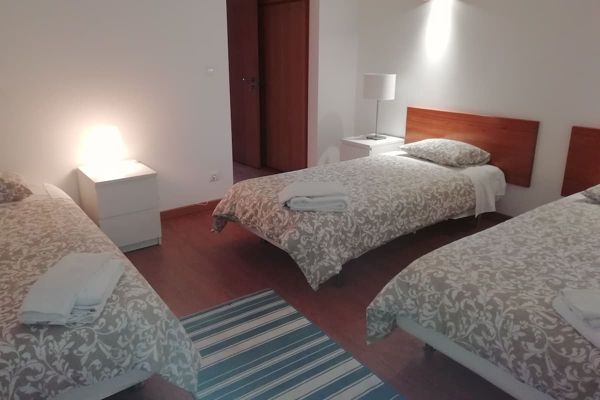 A hotel room with three beds, a wooden headboard, a nightstand with a lamp, and a striped rug.