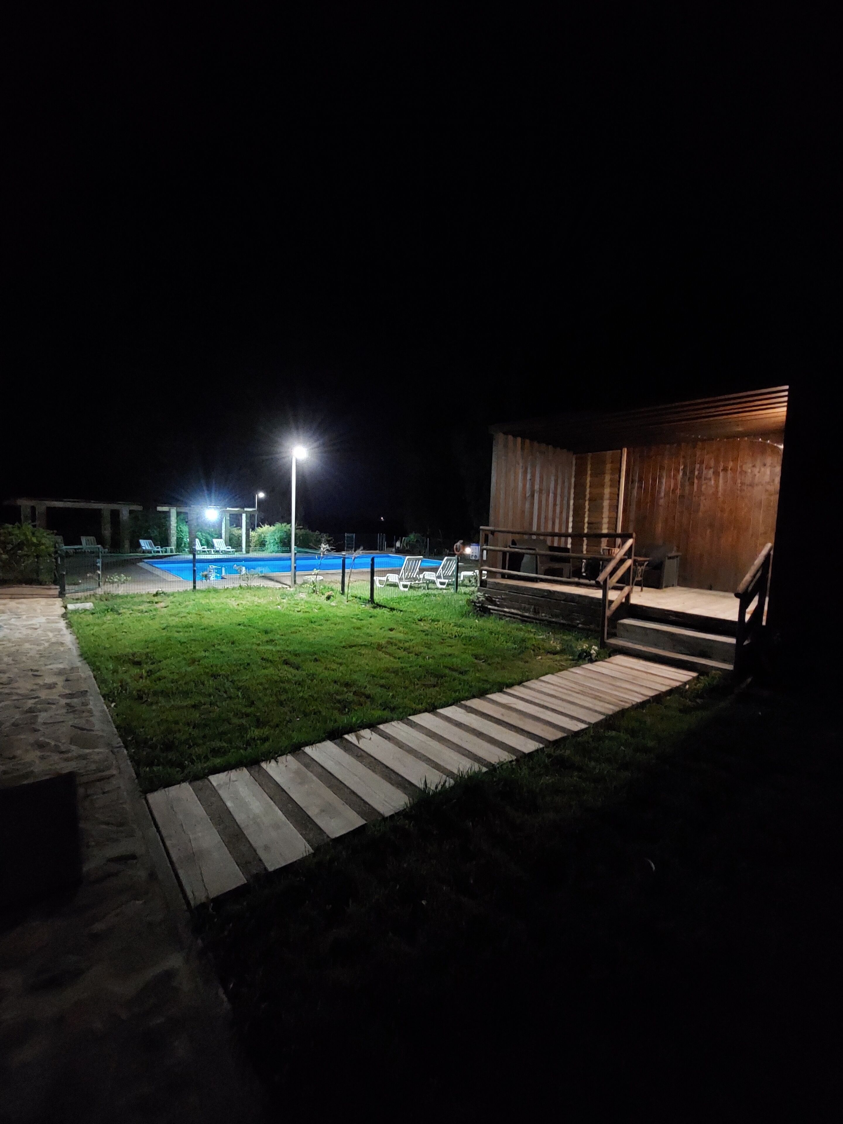 Ein Nachtbild von einem Poolbereich mit einer Holzterrasse und Treppen, die zu einem Gebäude führen.
