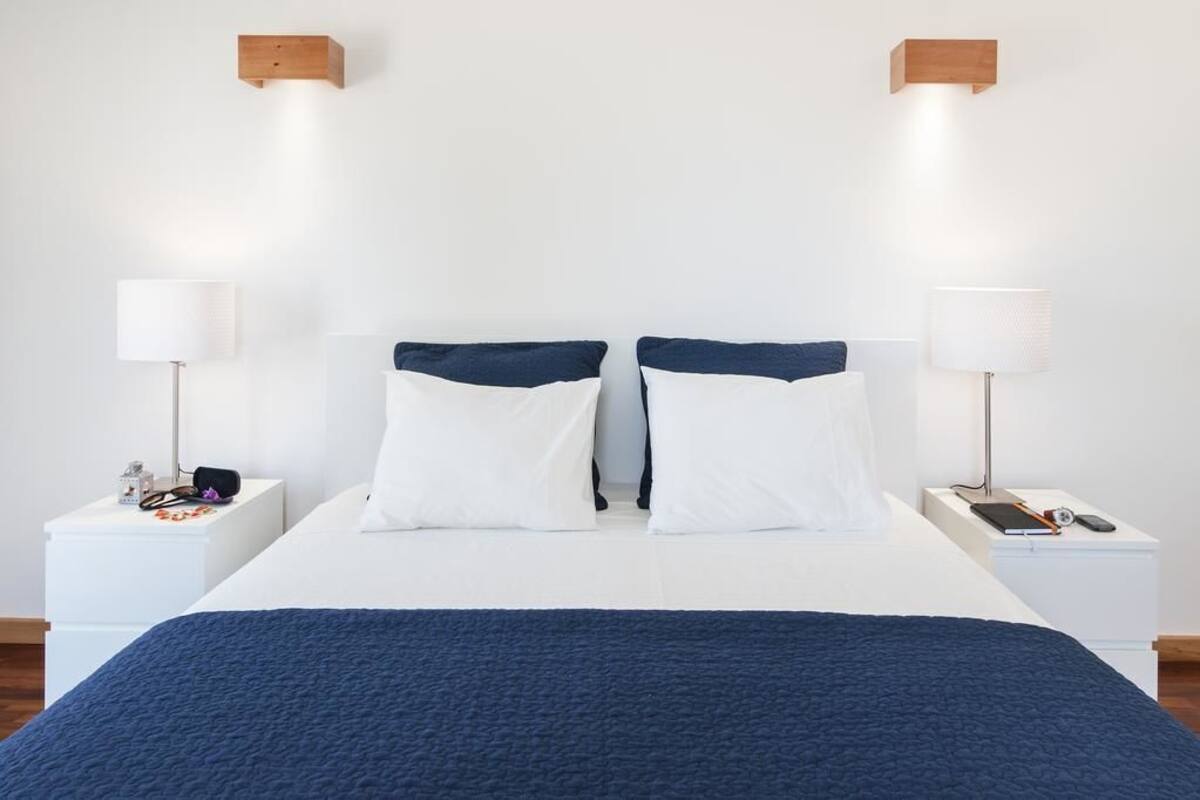 A neatly made bed with white and navy bedding, two bedside tables with lamps, and a wooden headboard.