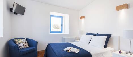 A bedroom with a bed, bedside tables, a chair, a TV mounted on the wall, and a window with a view of the outdoors.