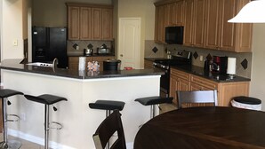 Une cuisine moderne avec des meubles en bois, un îlot central doté de tabourets, un réfrigérateur, un four à micro-ondes et une cuisinière.