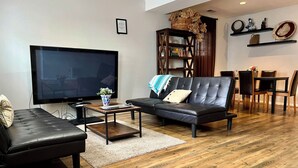 Una sala de estar moderna con un sofá de cuero negro, un televisor de pantalla plana, una mesa de centro y una estantería.