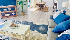 Ein modernes Wohnzimmer mit Fernseher, einer Couch, einem Couchtisch und einem Essbereich mit Tisch und Stühlen.